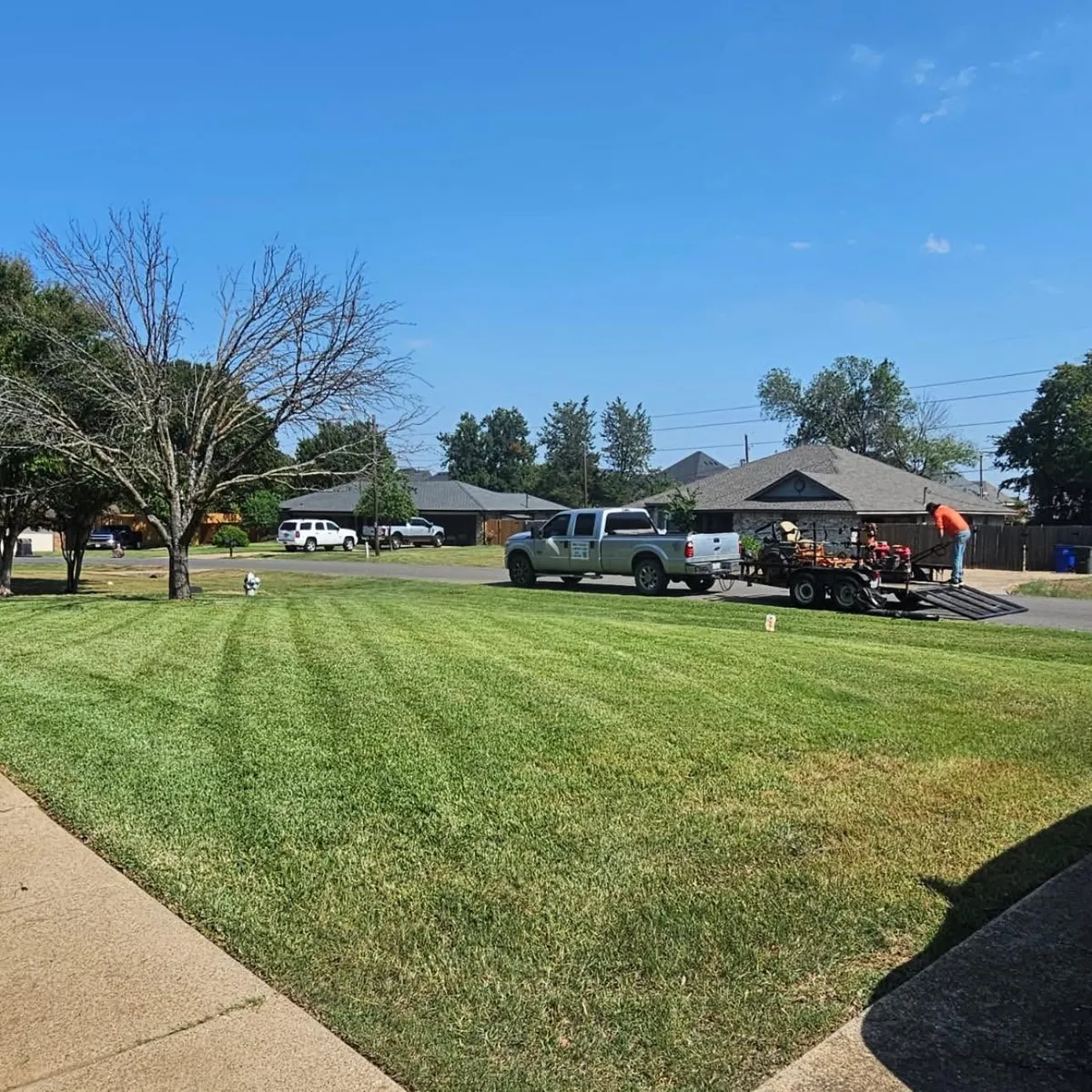 Corner-lot lawn freshly striped, with the Brothers truck and trailer at the curb.